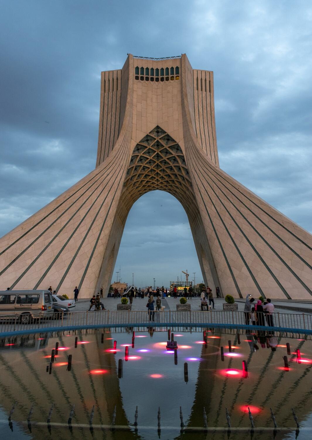 برجِ آزادیِ تهران در نورِ غروب، مردمی گِردِ حوضِ نورپردازی‌شدهٔ میدان.