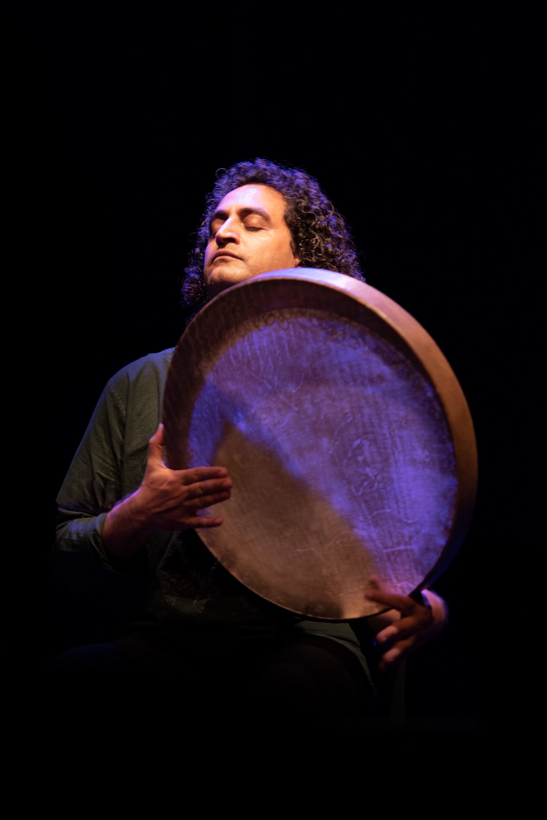 Musician Reza Samani playing the large Persian/Kurdish daf frame drum under blue stage light