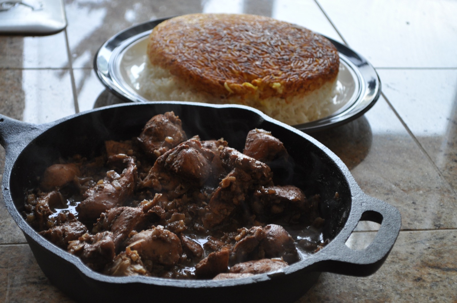 A pot of fesenjan — chicken in pomegranate-walnut sauce — beside a plate of crispy tahdig rice