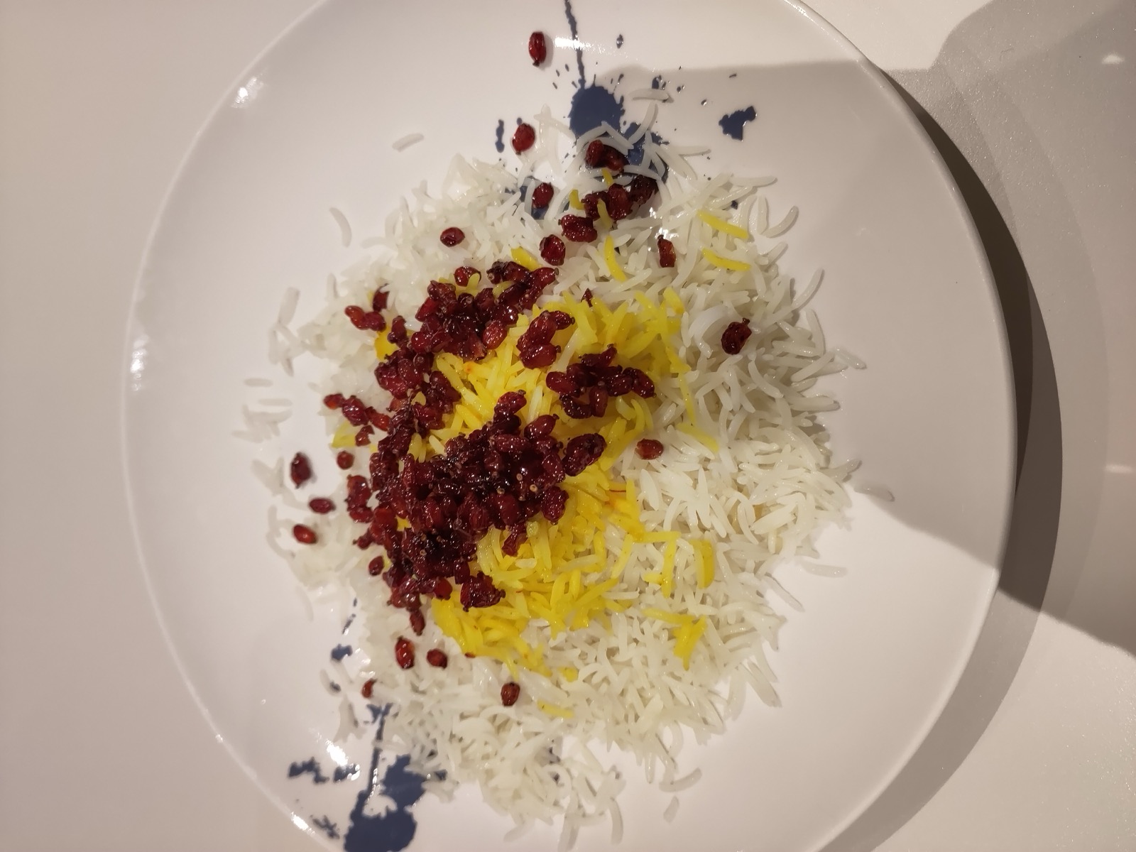 A plate of white and saffron rice topped with a mound of dried barberries (zereshk)