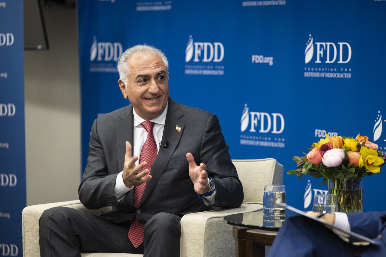 Reza Pahlavi seated in an armchair, speaking with open hands during a fireside chat, 2025
