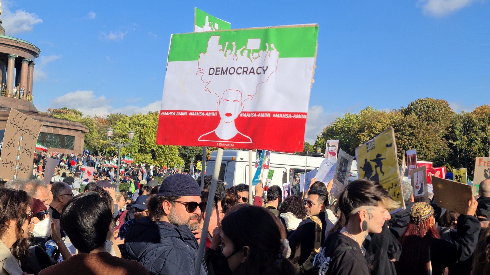 A protest placard in the shape of the Iranian Lion-and-Sun flag reads 'Democracy' over Mahsa Amini's face at the Berlin rally.